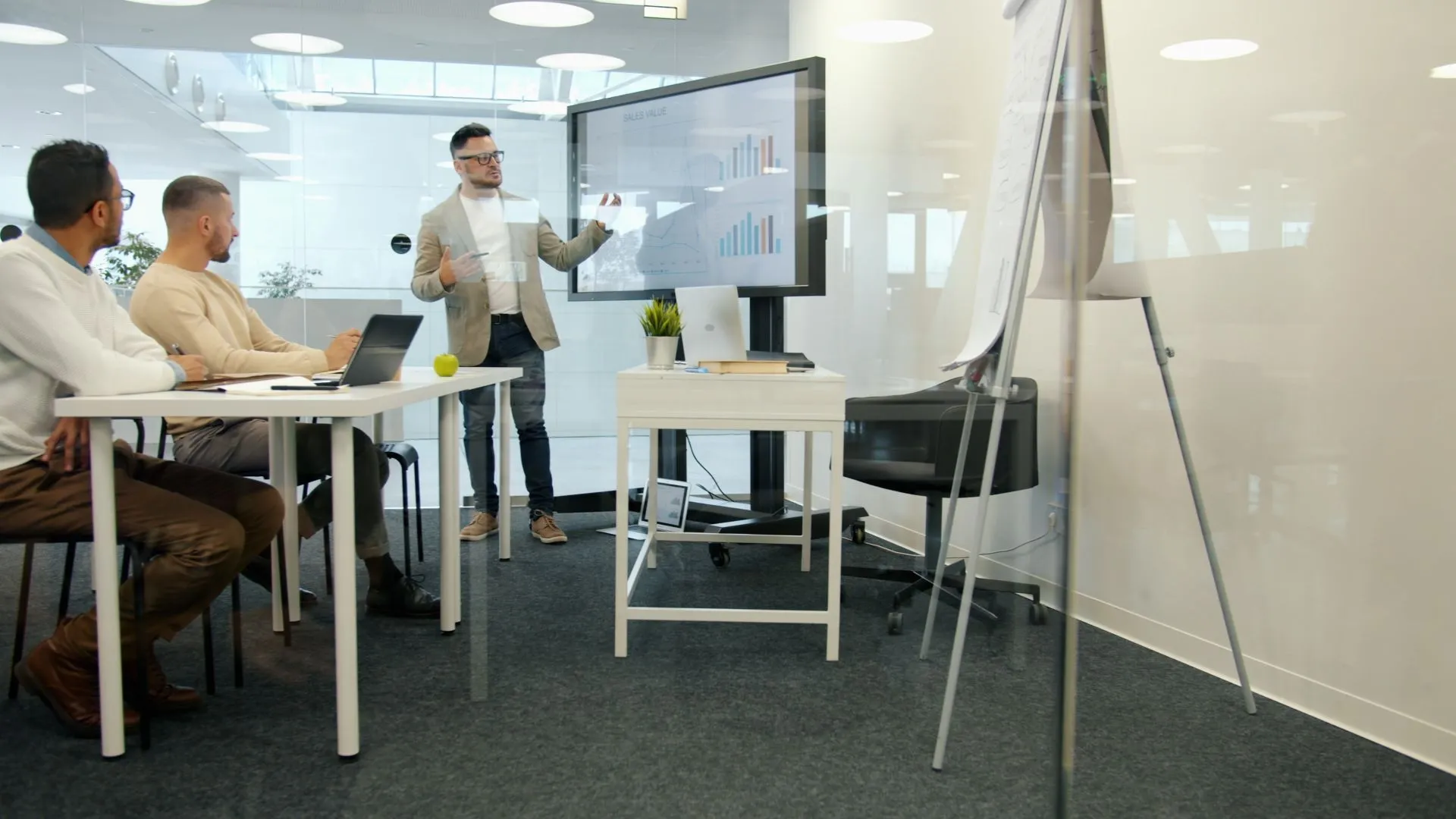 Un formateur présente des graphiques sur grand écran à des participants dans un bureau lumineux